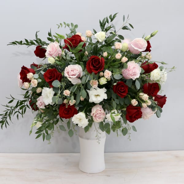 Tall vase of red, pink, and white roses with filler blooms in a lush, wide arrangement