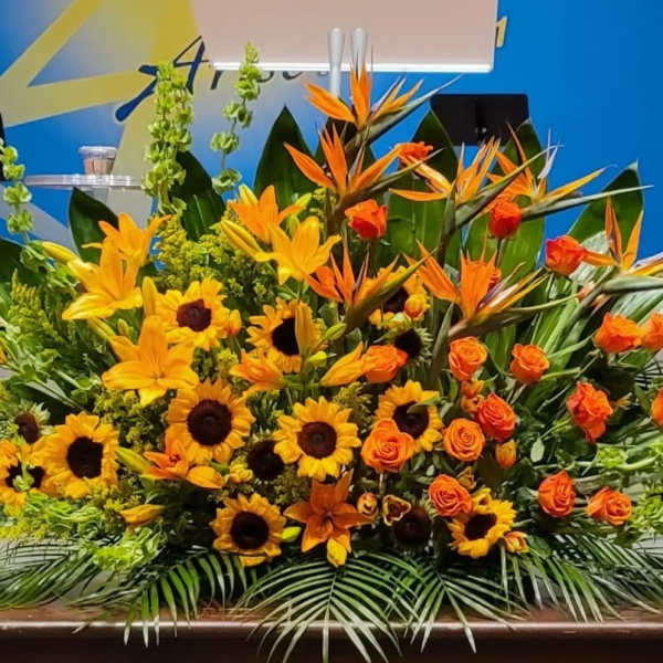 Large yellow and orange altar-style flower arrangement with sunflowers, lilies, roses, and birds of paradise.
