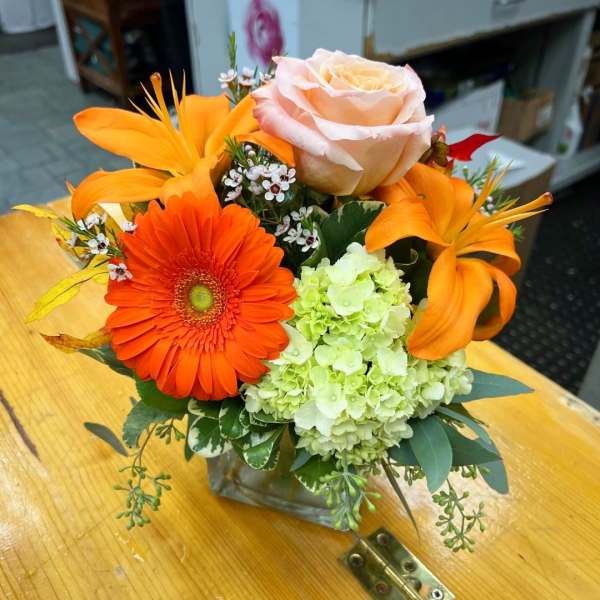 Orange gerbera, peach rose, and green hydrangea arrangement in a glass vase