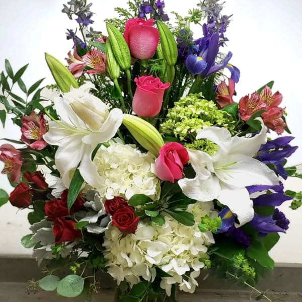 Tall mixed bouquet with white lilies, pink roses, and purple flowers in a glass vase