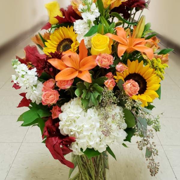 Large mixed bouquet with sunflowers, lilies, roses, and white hydrangeas in a glass vase