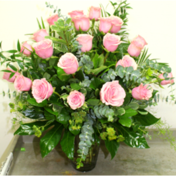 Pink roses arranged in a clear glass vase with greenery