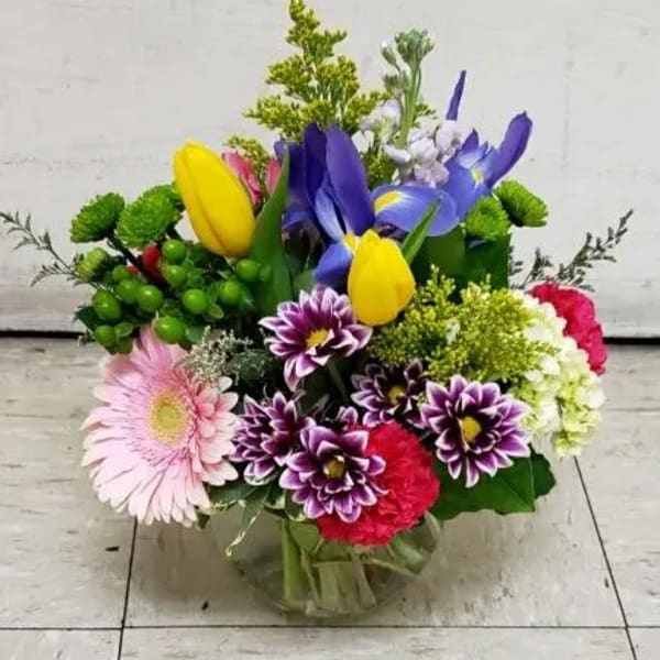 Colorful mixed bouquet with tulips, irises, daisies, and carnations in a glass vase