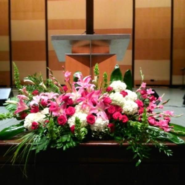 Low altar floral arrangement with pink lilies, red roses, and white blooms in front of a podium