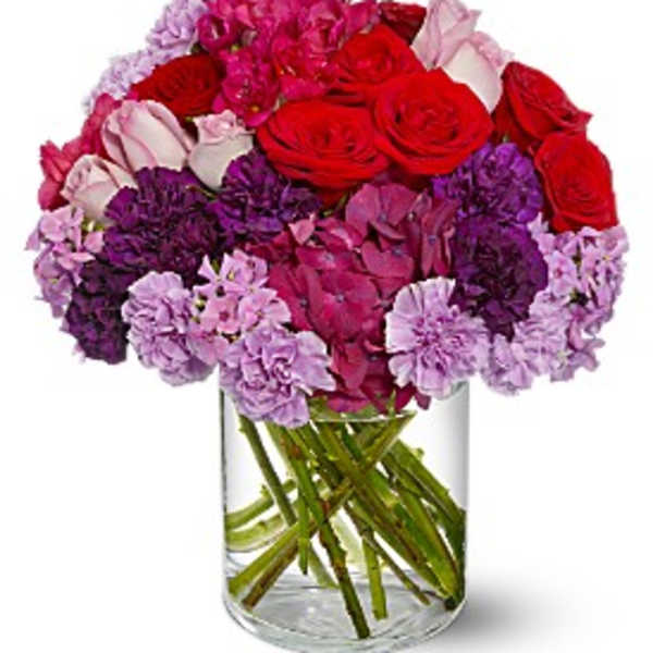 Bouquet of red roses and pink-purple carnations in a clear glass vase