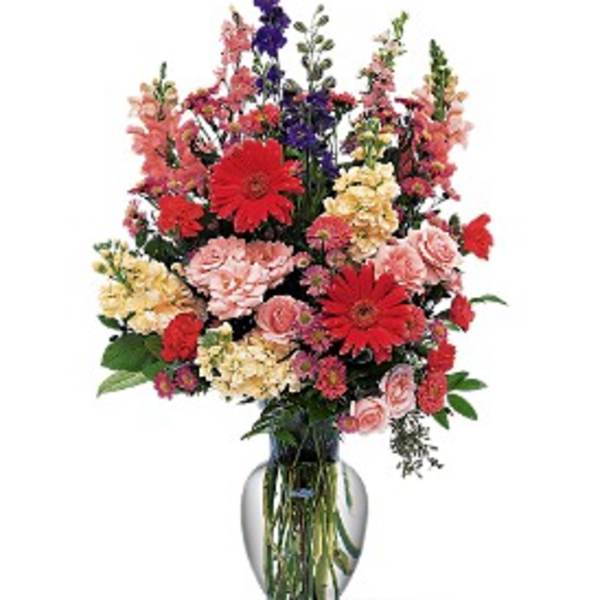 Mixed bouquet of red, pink, yellow, and purple flowers in a clear glass vase