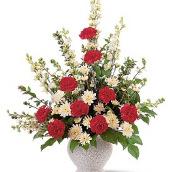 Tall arrangement of red carnations and cream chrysanthemums in a white urn vase