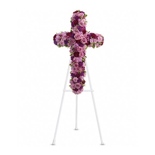 Standing floral cross of pink and purple blooms displayed on a white easel.