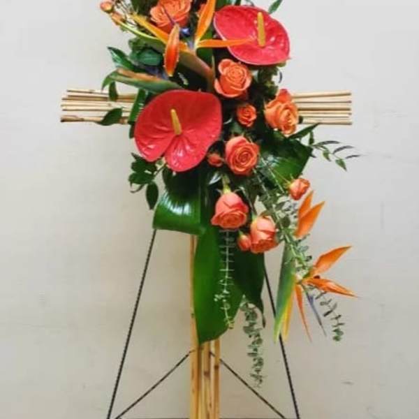 Tall bamboo cross spray with orange roses, red anthuriums, and birds of paradise on a stand