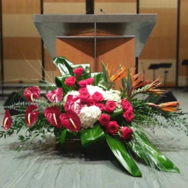 Large red and white podium floral arrangement with roses, hydrangeas, and tropical blooms on a stage