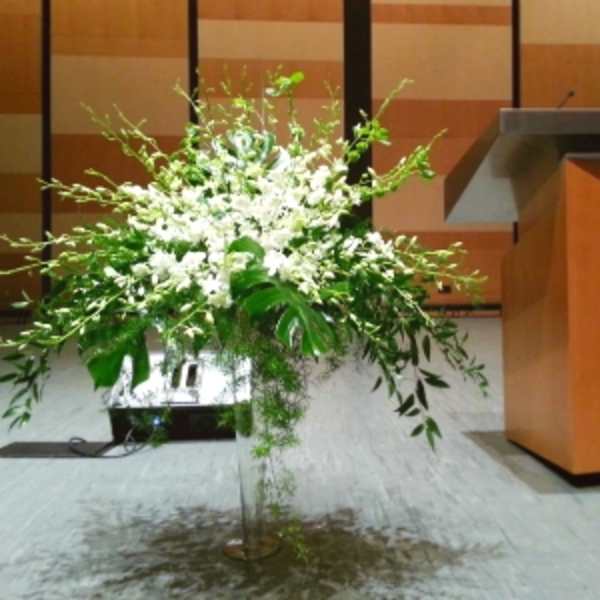 Tall white floral arrangement in a clear vase at a podium