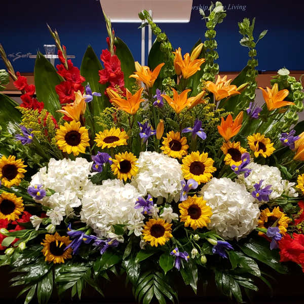 Large altar-style arrangement with sunflowers, white hydrangeas, orange lilies and mixed bright flowers