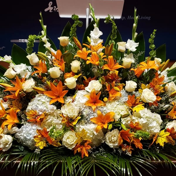 Large altar-style arrangement of orange lilies and white roses with hydrangeas in a low horizontal design