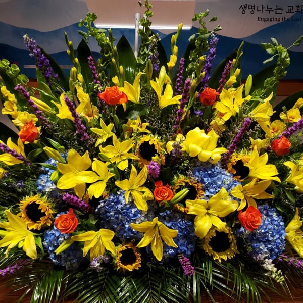 Large floral arrangement with yellow lilies, blue hydrangeas, and orange roses