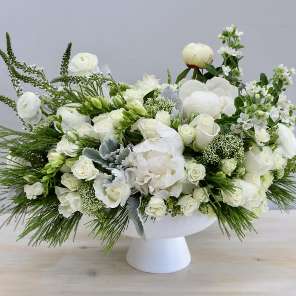 Low white pedestal arrangement with white roses, peonies, and other white blooms