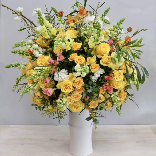 Tall arrangement of yellow roses with white and pink flowers in a white vase