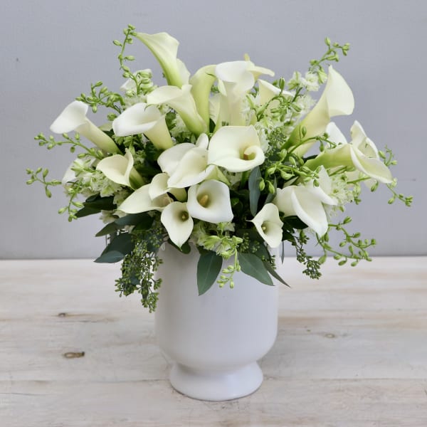 Arrangement of white calla lilies in a white pedestal vase