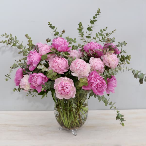 Large arrangement of pink peonies with eucalyptus in a clear glass vase