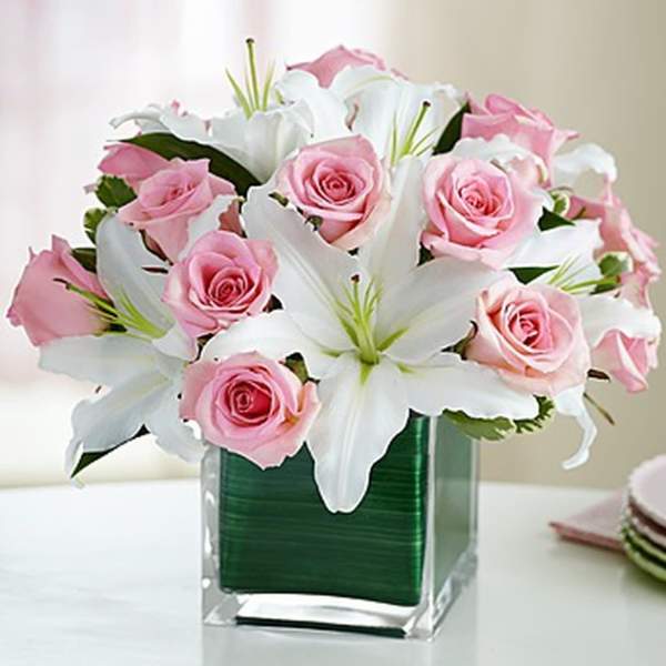 Pink roses and white lilies arranged in a clear square vase