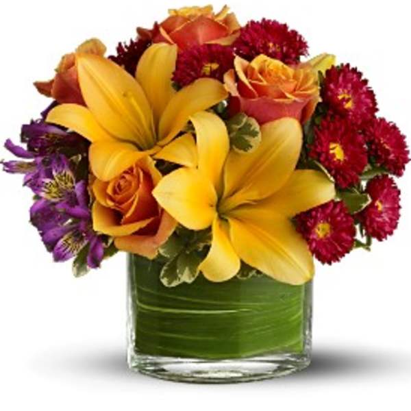Bouquet of yellow lilies, orange roses, and red daisies in a glass vase