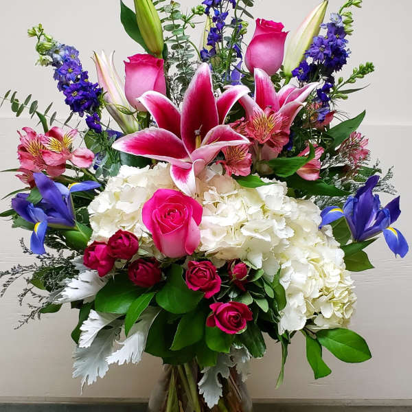Tall mixed bouquet with pink lilies, roses, hydrangea, and blue iris in a glass vase