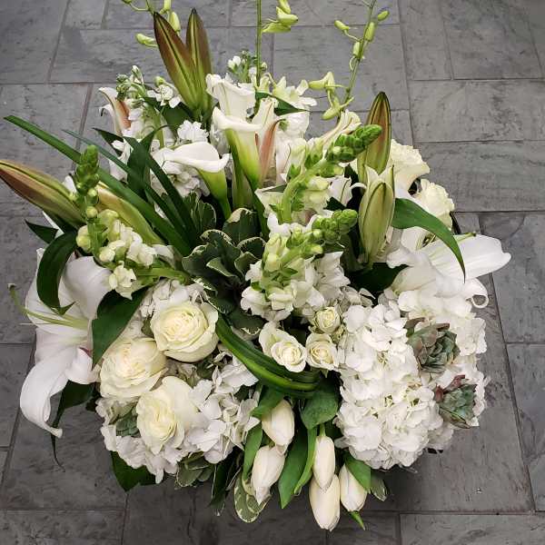 White floral arrangement with lilies, roses, and calla lilies in a low design