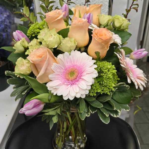 Bouquet of peach roses, pink gerbera daisies, and purple tulips in a glass vase