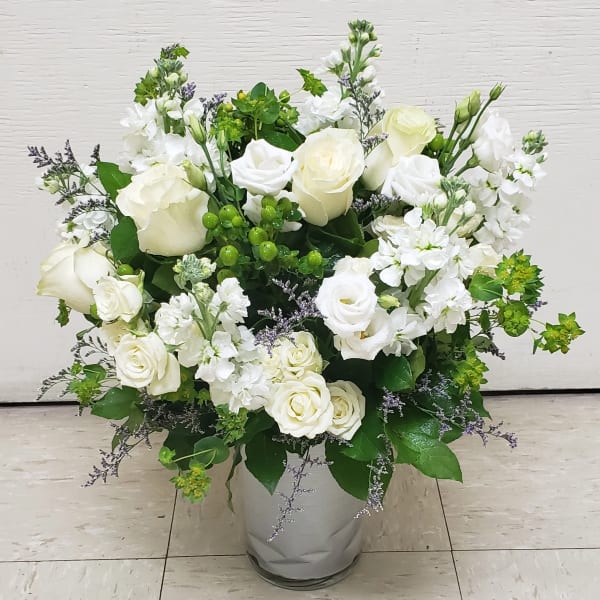 White roses and white stock in a glass vase with green accents