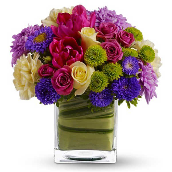 Mixed bouquet of roses, tulips, and daisies in a clear square vase