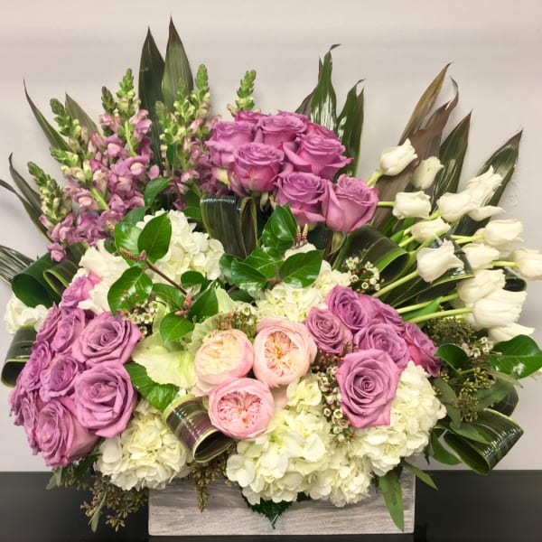 Low rectangular arrangement with lavender roses, white hydrangeas, pink roses, and white tulips.