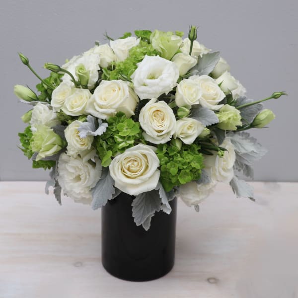 Compact arrangement of white roses and lisianthus with green blooms in a black cylinder vase