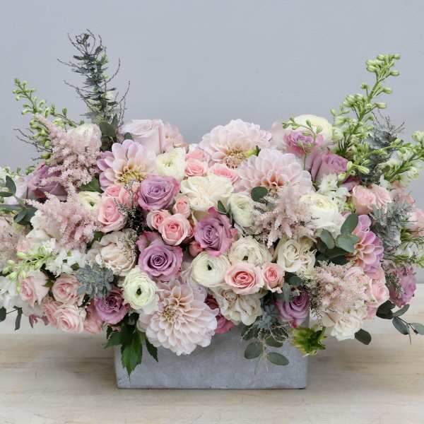 Low pastel arrangement of roses, dahlias, and ranunculus in a rectangular stone container