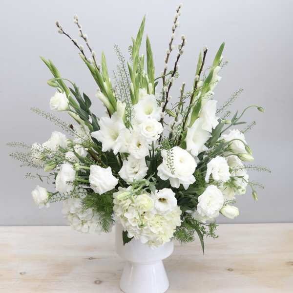 Tall white flower arrangement with lisianthus and ranunculus in a white pedestal vase