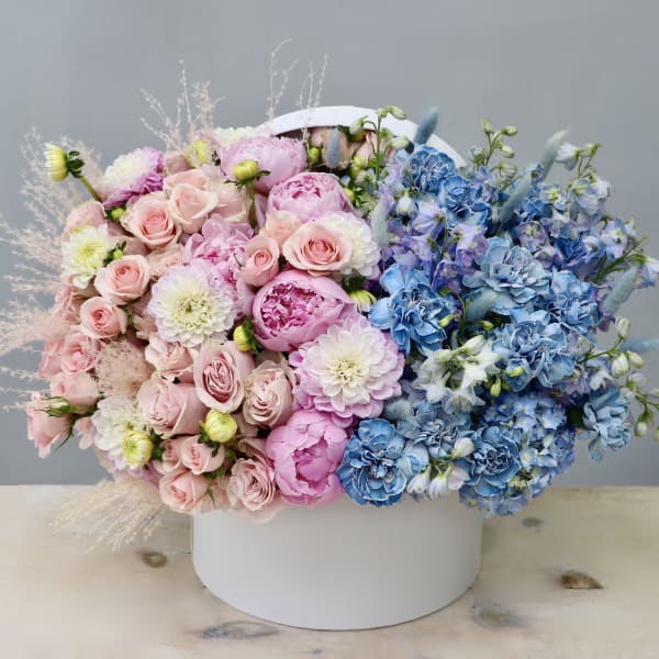Large hatbox arrangement of pink roses and peonies with blue and white blooms in a split-color design