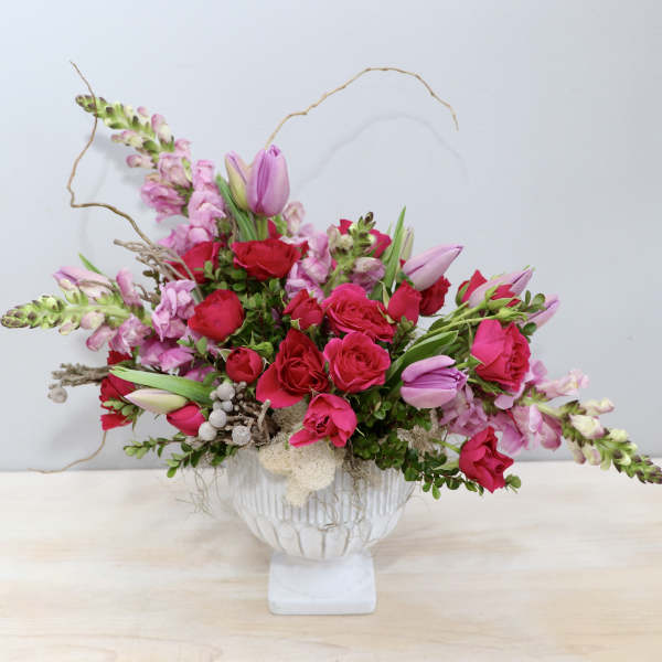 Asymmetrical arrangement of bright pink roses and tulips in a white pedestal vase