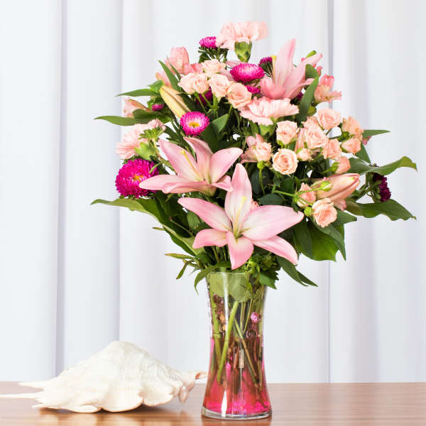 Tall bouquet of pink lilies, carnations, and spray roses in a clear vase with pink water