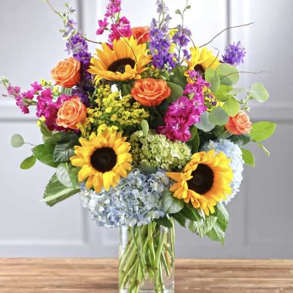 Mixed bouquet with sunflowers, roses, hydrangeas, and purple blooms in a glass vase