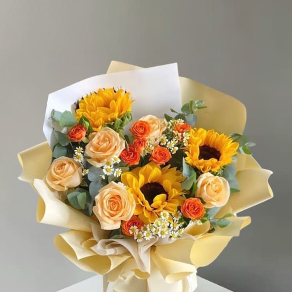Bouquet of sunflowers, peach roses, and orange spray roses wrapped in cream paper