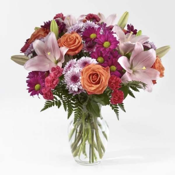 Mixed bouquet of lilies, roses, carnations, and mums in a clear glass vase