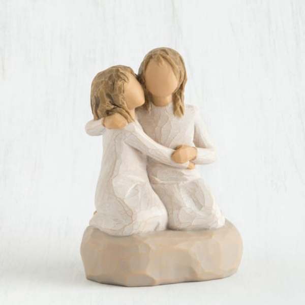 Two faceless figurines in white dresses embracing on a beige base