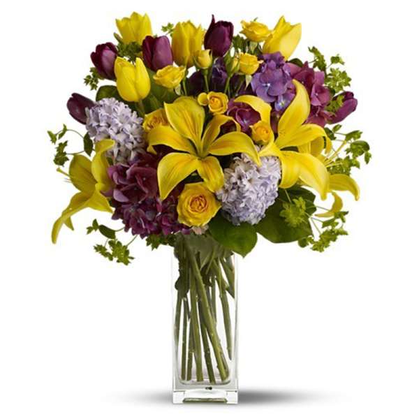 Bouquet of yellow lilies, purple flowers, and roses in a clear glass vase