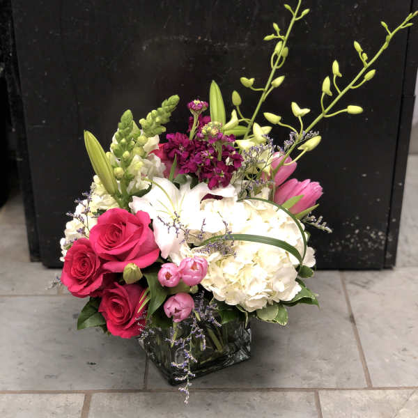Pink roses and white lilies in a glass vase with hydrangea and orchids