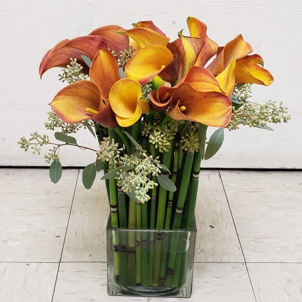Orange and yellow calla lilies in a square glass vase