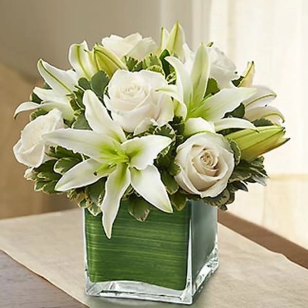 White lilies and roses arranged in a square glass vase