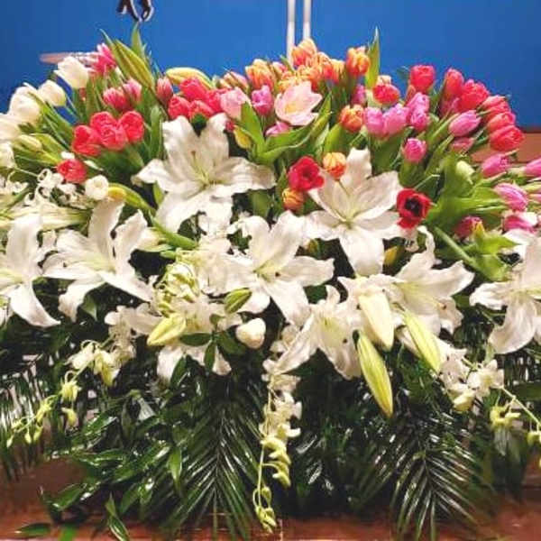 Low spray of white lilies with pink and red tulips arranged in a wide display on a stage.