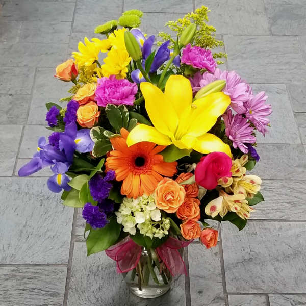Colorful mixed bouquet in a clear glass vase with a pink ribbon