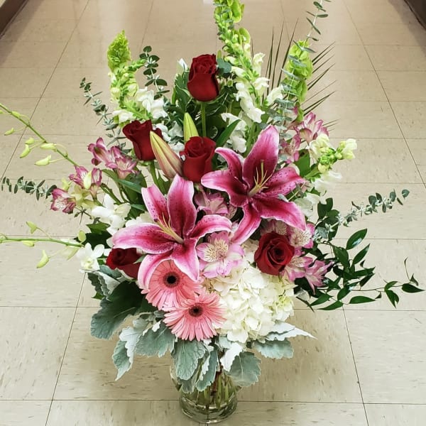 Tall bouquet of pink lilies, red roses, and white blooms in a glass vase