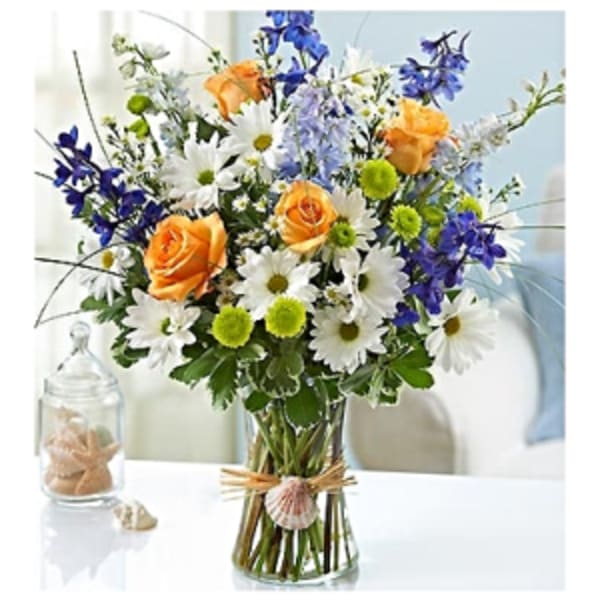 Bouquet of orange roses, white daisies, and blue flowers in a glass vase