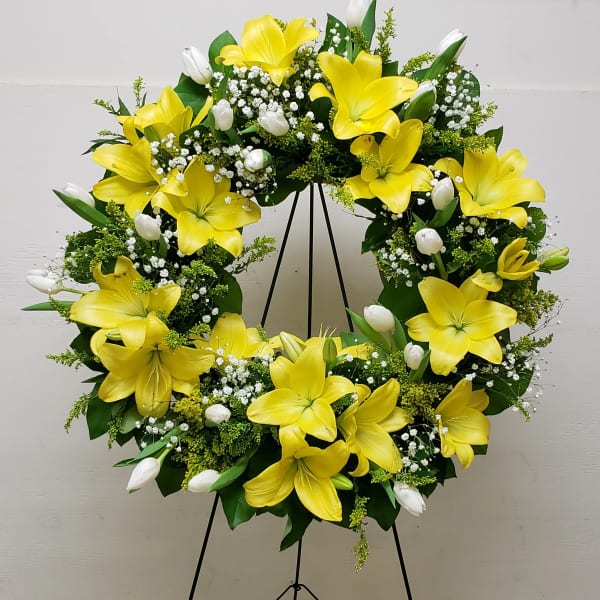 Standing wreath of yellow lilies and white tulips arranged in a ring on a metal easel
