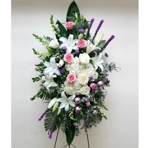 Tall standing spray of white lilies, hydrangeas, and pink roses with purple accents on an easel